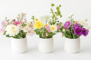 Three simple vases display delightful, fresh flower bouquets against a bright, neutral background photo