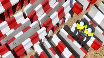 view of two construction workers in safety gear using a laptop at a worksite surrounded by red and white barricades, showcasing teamwork, planning, and efficient use of technology in construction photo
