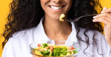 Healthy Diet. Unrecognizing Woman Holding Bowl With Vegetable Salad And Fork, Eating Dieting Food, Enjoying Organic Vegetarian Meal, Standing Over Yellow Background In Studio, Cropped Image, Closeup photo