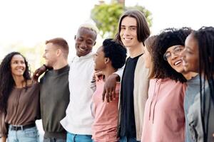 International group of friends in casual outfits smiling and embracing on the street, carefree multiracial students standing in a row and hugging outdoors, having conversation, closeup, panorama photo