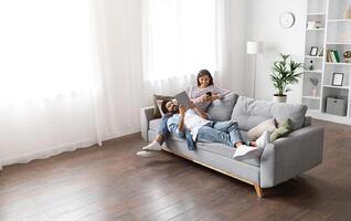 Gadget addiction, modern technologies and millennials lifestyle. Beautiful mixed race spouses resting on sofa at home, using digital tablet and smartphone, high angle view, copy space photo
