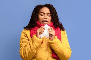 Cold And Flu. Sick Black Woman Sneezing In Paper Handkerchief Standing Over Purple Studio Background, Suffering Rhinitis And Sinusitis. Autumn And Winter Influenza Season, Healthcare Concept. photo