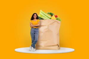 A customer stands confidently next to a large paper bag brimming with colorful vegetables and fruits. The bright background emphasizes the joy of shopping for groceries in today's market. photo