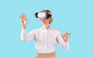 Business lady in VR headset touching virtual screen on blue studio background. Female entrepreneur exploring augmented reality, performing work related activities, playing game in cyberspace photo
