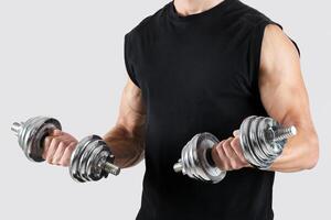 Unrecognizable millennial bodybuilder working out with dumbbells, pumping iron over light studio background. Closeup of motivated young sportsman lifting weights, doing strength exercises photo