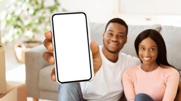 Positive black guy showing house key and his wife smiling in new home, selective focus. Millennial African American couple happy to move to bigger apartment, space for text photo