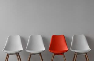 Three white chairs and red on gray wall background in office or room. Row of stools with one of different colour. Job opportunity, recruitment, business, leadership and hiring concept, copy space photo