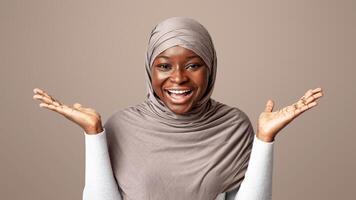 Happy black muslim lady in hijab spreading hands in excitement, exclaiming in amazement, glad to see somebody, experiencing happy shock, standing over light studio background with copy space photo