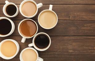 Border of various kinds of coffee in cups of different size on rustic wooden table, top view, copy space photo