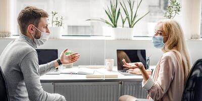 Discussion of work issues and creative ideas between colleagues through glass board at work. Busy woman and man in protective masks talking at workplace in modern office during covid outbreak photo