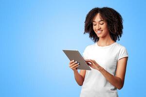 Working online, dating and chatting on self-isolation. Cheerful young african american lady with curly hair surfing in internet in tablet and typing message isolated on purple background, empty space photo