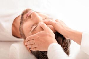 Peaceful bearded man getting healing head massage at modern luxury spa, top view. Spa therapist or cosmetologist making relaxing massage for handsome middle aged man, rubbing his forehead photo