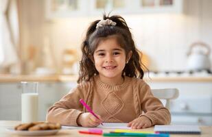 Cute Smiling Little Girl Drawing In Kitchen Interior, Adorable Female Kid Child Sitting At Table With Cookies And Milk At Home And Looking At Camera, Closeup Portrait With Copy Space photo
