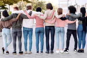 Back view of multiracial millennial demonstrators in casual standing in a row on the street, embracing, making live chain, fighting fot human rights, defying lockdown restrictions, panorama photo