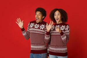 Shock and unexpected meeting. Amazed millennial african american male and female express positive emotions of surprise, gesturing and looking at empty space, isolated on red background, studio shot photo