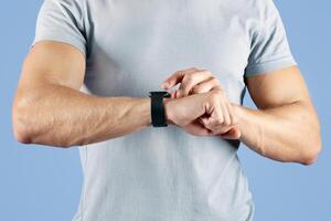 Unrecognizable young sportsman checking his smartwatch on violet studio background, closeup. Cropped view of millennial athlete using fitness tracker while exercising. Modern technologies in sports photo