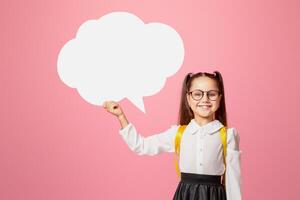 Got an idea. Smiling schoolgirl in uniform with backpack holding abstract bubble with free space, isolated on pink background, studio shoot photo