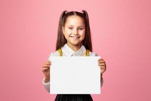 Primary education. Small schoolgirl with happy smile holding sign with free space, isolated on pink background, studio shoot photo