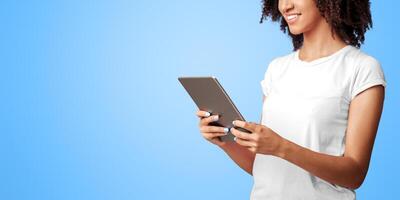 Work and relaxation with modern devices. Smiling young african american woman in pink t-shirt with curly hair, surfing on internet use digital tablet isolated on violet background, empty space photo