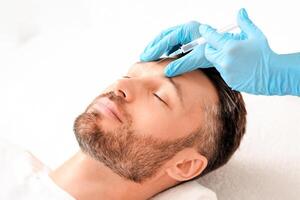 Unrecognizable cosmetologist in protective gloves injecting filler between mans eye brows against frown lines, closeup. Middle aged man getting lifting procedure at clinic, copy space photo