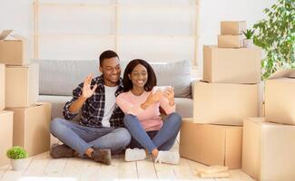 Positive millennial couple having call with friends or family on smartphone in their new home, waving to camera, copy space. Young newlyweds moving to their own apartment photo