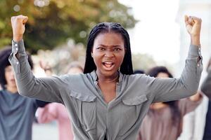 Black lady guiding multiracial group of activists, rasising fists up, showing unity and strength, millennial strikers different nationalities walking by street, protesting against discrimination photo