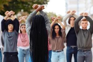 Unrecognizable long-haired black woman leading group of protestors striking for human rights, back view of lady standing in front of multiracial demonstrators raising fists up and crossing hands photo
