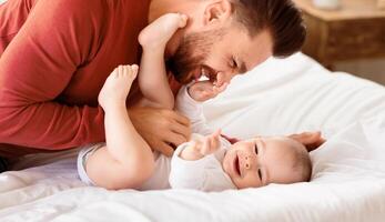 Cute Father Cuddling Bonding With Little Baby Daughter Spending Time Together Lying On Bed At Home. Loving Daddy Laughing Playing With Toddler. Fatherhood, Dad's Love, Child Care And Parenting Joy photo