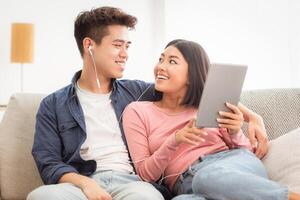 Chinese Family Couple Using Tablet Computer Watching Movie Online Sitting On Sofa At Home, Relaxing On Weekend. Asian Girlfriend And Boyfriend Enjoying Weekend Using Gadget App, Browsing Internet. photo