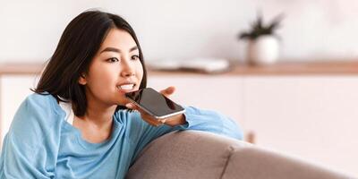 Phone Call, Mobile Communication And Voice Assistant Concept. Asian woman using cellphone audio recognition to send message, holding gadget near mouth. Lady talking on mobile loudspeaker photo