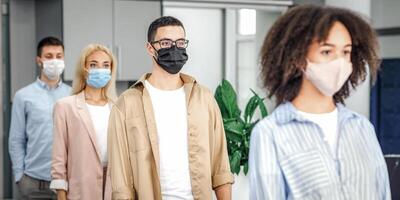 Queue to check temperature before work and new normal after lockdown and social distancing. Multiracial workers in protective masks near office entrance on job during coronavirus epidemic photo