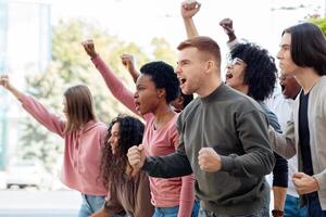 Side view of multiracial group of students chanting slogans and showing fists during demonstration, fighting against reforms in education, copy space. Students rally, demonstration, strike concept photo