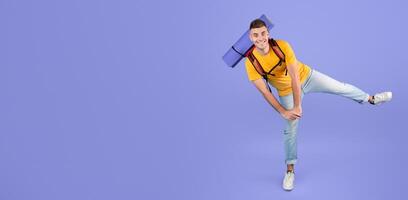 Full length portrait of happy young man with camping equipment dancing over blue studio background. Millennial male traveler excited to go hiking, trekking or mountaineering. Tourism concept photo
