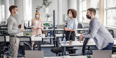 Modern team meeting, group work and social distancing. Manager with tablet speaks with workers in protective masks in interior of modern office with gadgets during coronavirus epidemic, free space photo
