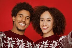 Selfie photo of couple on smartphone and celebrating new year and christmas during self-isolation in quarantine covid-19. Happy male and female in sweaters looking at camera isolated on red background