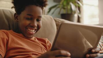 This boy is smiling and engaged in a call using a tablet while sitting comfortably indoors. photo