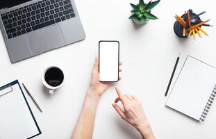 Woman hands using cellphone in office while working, copy space, top view, blank screen photo