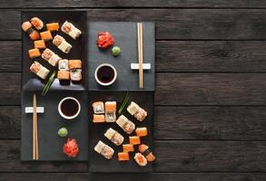 Japanese food restaurant, sushi maki gunkan roll plate or platter set. Copyspace with chopsticks, ginger and wasabi. Sushi at rustic wood background and black stone. Top view at black. Flat lay. photo