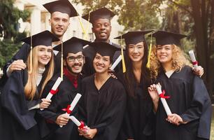 Multiethnic students taking group photo to celebrate their graduation day, copy space. Education, qualification and gown concept.
