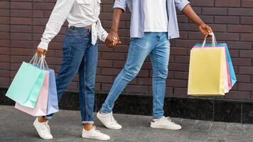 Shopping in mall on weekends. African american couple with multicolored bags go away from store, outdoors, free space photo