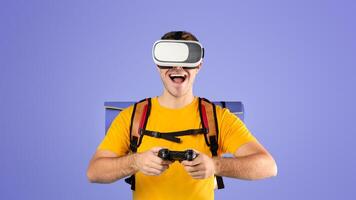 Virtual tourism. Excited millennial guy with VR headset and controller watching travel tour in cyberspace over blue studio background. Happy young man having vacation or journey in augmented reality photo