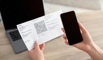 Woman using mobile phone to scan the QR code for the bill through the app, smartphone with blank screen. Paying online from home. Stay safe and have social distance photo