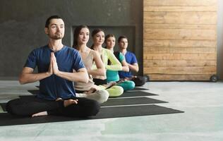Young women and men in yoga class, meditation exercises. Lotus pose for relaxation. Healthy lifestyle in fitness club, crop, copy space, selective focus photo