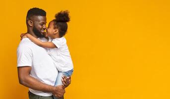 Happy family. Adorable little african girl touching noses with her daddy, orange panorama background with empty space photo