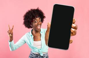 Great App. Cheerful Excited Black Woman Holding Smartphone With Blank Screen And Gesturing Peace, Funny African American Female Recommending New Mobile Application Or Website, Mockup Image photo