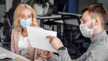 Working with graphs and diagrams during social distance in modern office. Busy young man and woman managers in protective masks work with documents through glass board during coronavirus epidemic photo