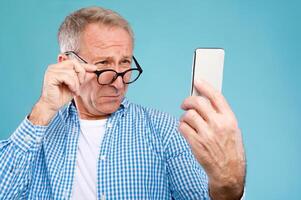 Poor Eyesight. Senior Man Squinting Eyes Reading Message On Phone Wearing Eyeglasses Having Problems With Vision, Blue Studio. Ophtalmic Issue, Bad Sight In Older Age, Macular Degeneration Concept photo