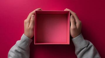 Hands grasp an empty, open box with a textured interior, placed on a bright pink surface. The moment captures the anticipation of receiving a delivery, highlighting the excitement of unboxing. photo