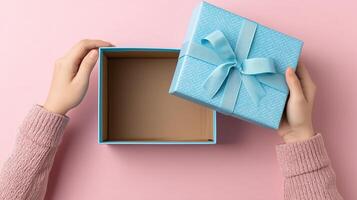 Hands are holding a light blue gift box with a ribbon, revealing the inside of the empty container. The pink background contrasts with the box, making the moment visually appealing. photo