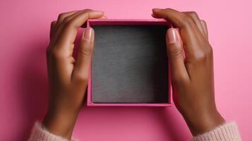 Hands grasp a small, open box against a vibrant pink backdrop. The box is empty and showcases a textured interior, indicating it was recently delivered. photo